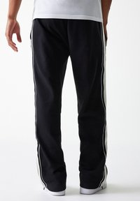 Pantalones de chándal negros con franjas laterales blancas, hechos de una tela suave, con un corte relajado y puños acanalados en los tobillos.