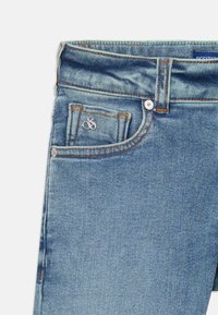 Jean en denim bleu clair avec un design à cinq poches, des détails de couture subtils et un petit logo en argent sur la poche avant.