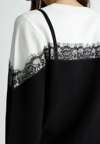 Haut noir et blanc avec une bordure en dentelle noire le long de la couture de l'épaule et une texture de tissu lisse. Design simple avec des détails de couture apparente.