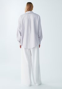 Lila gestreiftes Langarmhemd mit Kragen und abgerundetem Saum. Weiße weit geschnittene Hose mit glatter Textur.