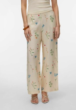 Beige bukser med vide ben og små farverige blomsterprint, båret med en cremefarvet ærmeløs top, sandaler, et brunt armbånd og en sølvring.