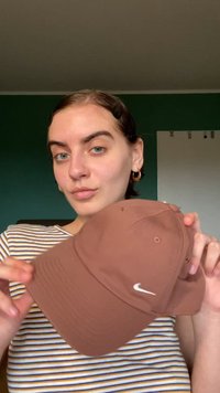 Καφέ καπέλο Nike με καμπυλωτό γείσο και άσπρο λογότυπο, κατασκευασμένο από υφασμάτινη υφή. Το μοντέλο κρατά το καπέλο, αποκαλύπτοντας λεπτομέρειες ραφής.