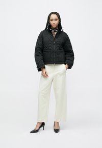 Czarna pikowana kurtka z wysokim kołnierzem i zamkiem z przodu, z dwoma przednimi kieszeniami. Do tego białe, szerokie spodnie i czarne szpilki.