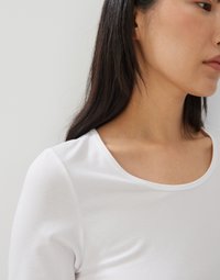 Witte lange mouwen top met een ronde hals en een gladde textuur, voorzien van passende mouwen en een minimalistisch ontwerp.