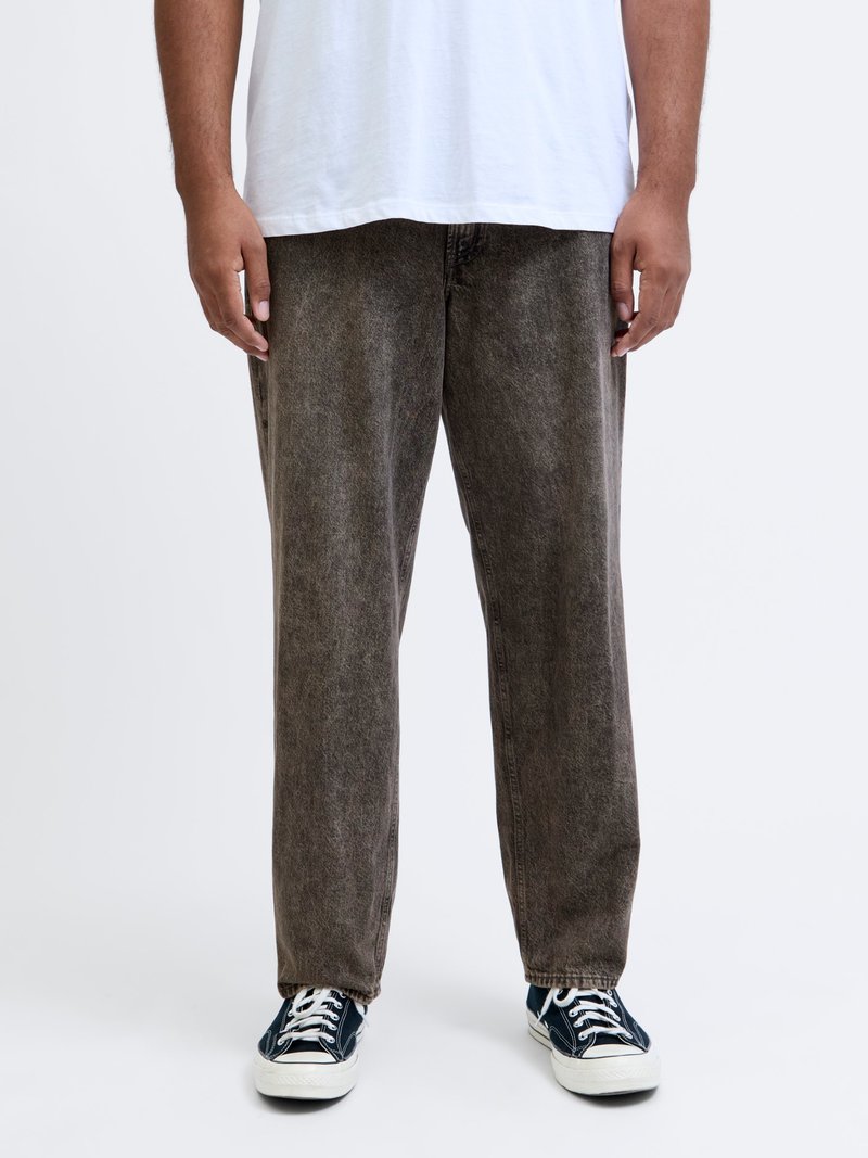 Stora bruna denimjeans med en blek textur, hög midja och raka ben, i kombination med svarta och vita sneakers.