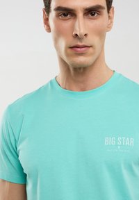 Gaiši tirkīza krāsas T-krekls, izgatavots no mīksta kokvilnas, ar apaļu kakla izgriezumu, īsām piedurknēm un uz krūtīm drukātu "BIG STAR" logo baltā krāsā.