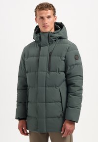 Donkergroen gewatteerde jas met een hoge kraag, voorzien van een ritsborstzak en een logo-patch op de mouw. Gladde textuur, warme uitstraling.