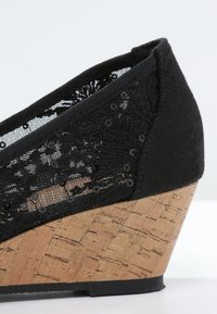 Escarpin noir à semelle compensée en liège, dessus en tissu en maille orné de sequins et de broderies florales.