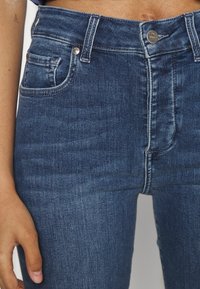 Džíny s vysokým pasem v tmavě modré barvě z denimové tkaniny s hladkou strukturou, vybavené předními kapsami a kovovými akcenty na knoflících.