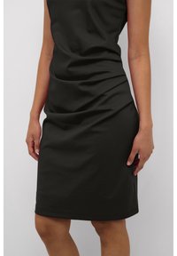 Svart figurnära klänning med en slät yta, ärmlös design och draperingar runt midjan, som når strax ovan knäna.