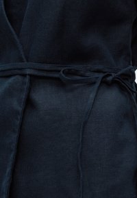 Σκούρο μπλε ύφασμα δεμένο στη μέση με μια λεπτή ζώνη σε έναν απλό κόμπο, που δείχνει την υφή και τις πτυχές του υλικού.