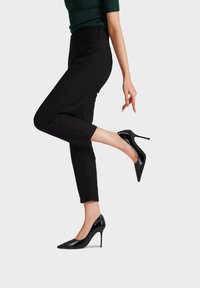 Pumps neri in vernice con tacco alto, punta affusolata, design elegante e tacco a stiletto, abbinate a pantaloni neri a mezza lunghezza.