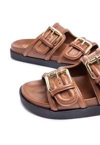 Brown leather slide sandals featuring two adjustable buckles, a smooth upper, and a black rubber sole for traction.