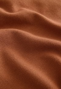 Tessuto di cotone in una calda tonalità marrone terroso con una superficie strutturata, caratterizzato da sottili motivi intrecciati e una morbida caduta.