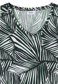 Haut à col en V avec motif de feuilles de palmier tropicales noir, blanc et vert, avec une étiquette de marque "CECIL" à l'intérieur de l'encolure.