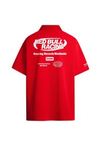 Sarkans īsām piedurknēm polo krekls, izgatavots no kokvilnas. Aizmugurē ir balts uzraksts: "RED BULL RACING" un citi zīmola detaļas. Klasisks apkakles dizains.