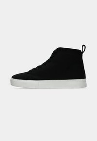 Svart høyhælte sneakers laget av semsket skinn med hvit gummisåle, med snøring og en liten trekkflik på hælen.