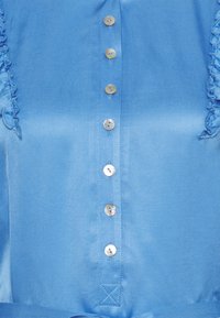 Light blue satin blouse with shiny pearl-like buttons down the center and small fabric ruffles along the front sides.