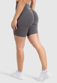 Graue hoch taillierte Shorts mit gerippter Textur und geschwungenen Nähten zur Hervorhebung. Getragen mit weißen Sportschuhen, vor einem einfarbigen Hintergrund.