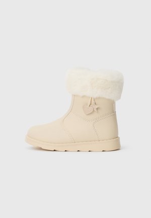 Winterlaars in crèmekleur met nepbonten boord, zijnaad en hangende bedeltjes in hart- en stervorm aan de buitenenkel.