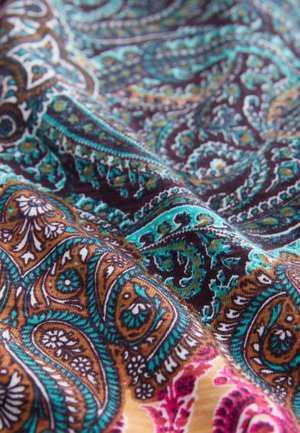 Krupan kadar šarenog tkanja s složenim paisley uzorcima u tirkiznoj, smeđoj, crnoj, bijeloj i ružičastoj boji, prikazujući teksturu i nabore.