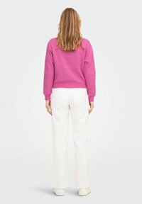Sudadera rosa con cuello redondo y puños acanalados, combinada con pantalones blancos de piernas anchas y zapatos blancos, vista desde atrás.