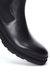 Bottine en cuir noir avec une texture lisse et brillante, des détails élastiques sur les côtés et une semelle en caoutchouc durable avec des rainures pour une meilleure traction.