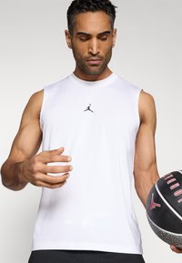 Haut de sport blanc sans manches en tissu évacuant l'humidité, avec un petit logo Jordan noir sur la poitrine.