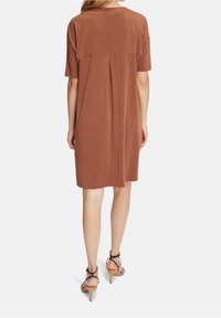 Brun klänning med kort ärm som har en avslappnad passform, pliserad ryggdetalj och kombineras med strapazierade högklackade sandaler.