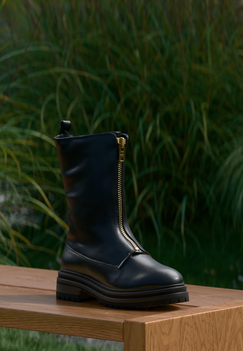 Botín de cuero negro hasta el tobillo con una cremallera dorada, suela de goma resistente y una textura suave. El diseño presenta una silueta elegante y moderna.