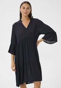 Rochie bleumarin din material ușor, cu decolteu în V, mâneci evazate și un design în straturi, cu o croială lejeră.