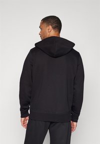 Schwarzer Kapuzenpullover mit weichem Material, gerippten Bündchen und Saum. Verfügt über eine Kängurutasche und einen lässigen Schnitt.