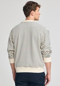 Męska kremowa bluza z poziomymi granatowymi paskami, z ribbowanymi mankietami i dolnym brzegiem, charakteryzująca się luźnym krojem i miękką teksturą. Widok z tyłu.