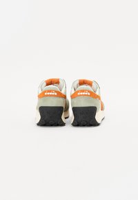 Sneakers with green suede upper, orange accents, and black textured rubber sole. Features a padded collar and logo detail on the heel.
