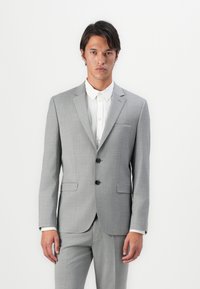 Light gray tailored suit with a textured fabric, single-breasted, two-button closure, notched lapels, and side pockets. Underneath, a white shirt.