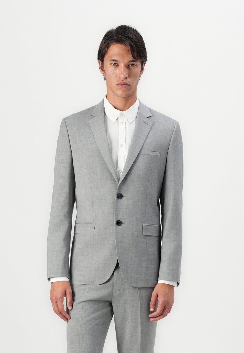 Light gray tailored suit with a textured fabric, single-breasted, two-button closure, notched lapels, and side pockets. Underneath, a white shirt.