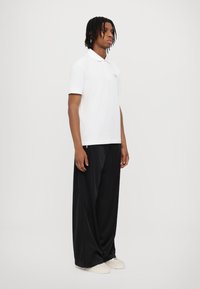 White polo shirt with a collar, worn with black wide-leg trousers. The fabric appears smooth and has a clean, minimalist design.
