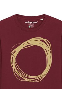 T-shirt à manches longues bordeaux avec un grand motif circulaire beige. Le tissu semble doux ; l'étiquette indique la composition du matériau et les instructions d'entretien.