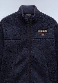 Marineblaue Fleecejacke mit hohem Kragen, Reißverschluss und zwei seitlichen Taschen. Verfügt über gestickte horizontale Blenden und einen Logo-Patch auf der Brust.