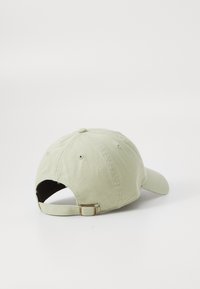 Light green baseball cap with adjustable strap laying on a white surface, viewed from the back and slightly to the side.