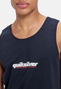 Tricou fără mâneci de culoare bleumarin, confecționat din bumbac, cu un decolteu rotund, având un logo alb și roșu pe piept.