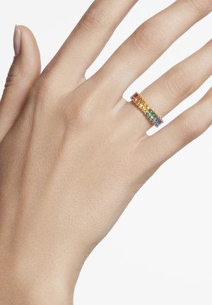 Gold ring with rectangular multicolored gemstones including pink, green, and blue. Features a textured band and a contemporary design.