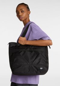 Svart tygväska gjord av nylon, med en geometrisk design och dragkedjestängning upptill. Väskan har dubbla handtag och en Vans logotyp. 