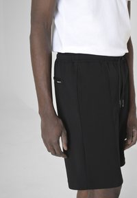 Pantaloni corti neri in cotone con un elastico in vita, tasche laterali e un accento argento nella tasca sinistra. Design semplice e aderente.
