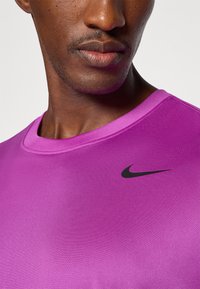 Nahaufnahme des unteren Gesichts und Halses einer Person, die ein leuchtend lila Nike-Shirt mit einem schwarzen Swoosh-Logo auf der Brust trägt.