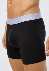 Svarta bomullsboxers med ett elastiskt midjeband med "Calvin Klein"-logotyp i ljusgrått. Designen är åtsittande med en slät textur.