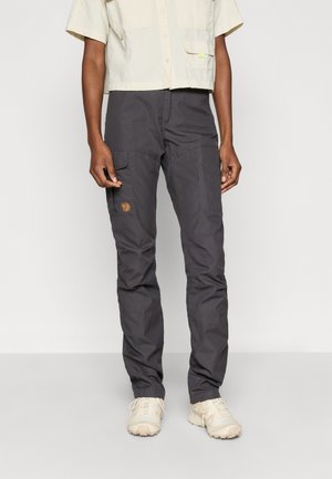 Person wearing dark gray cargo pants with logo patch on thigh and beige lace-up shoes, standing against plain light background.