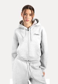 Felpa grigia con zip realizzata in un materiale morbido, dotata di tasca frontale, cappuccio con coulisse e logo ricamato sul lato sinistro.