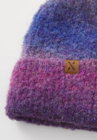 Pletená vlnená čiapka v purpurových a modrých odtieňoch s ohnutým okrajom a malou hnedou koženou značkou s vyrezávaným dizajnom "X".