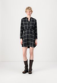 Rochie neagră cu model în grilă albă, mâneci lungi, închidere cu butoane în față, talie strânsă și tiv deasupra genunchiului. Purtați cu cizme maro până la genunchi.